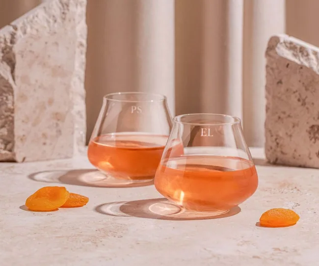 Two glasses of orange liquid on a stone surface with dried apricot slices and large stone pieces in the background.