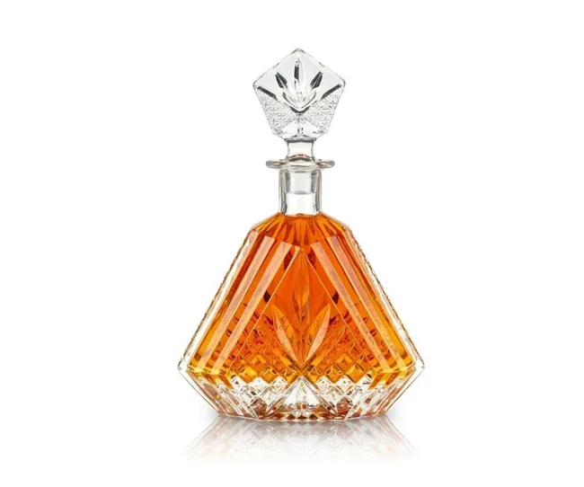 Artistic crystal decanter with amber liquid, featuring an intricate cut design and a geometric stopper.