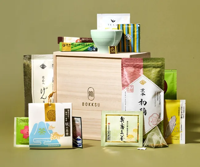 Assorted Japanese tea packages displayed with a wooden Bokksu box and a green teacup on top.