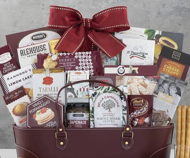 Gift basket with assorted snacks, crackers, chocolates, and olives, featuring a large red bow.