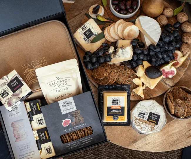 Cheese and cracker platter with olives, figs, and Maggie Beer products set on a wooden table.