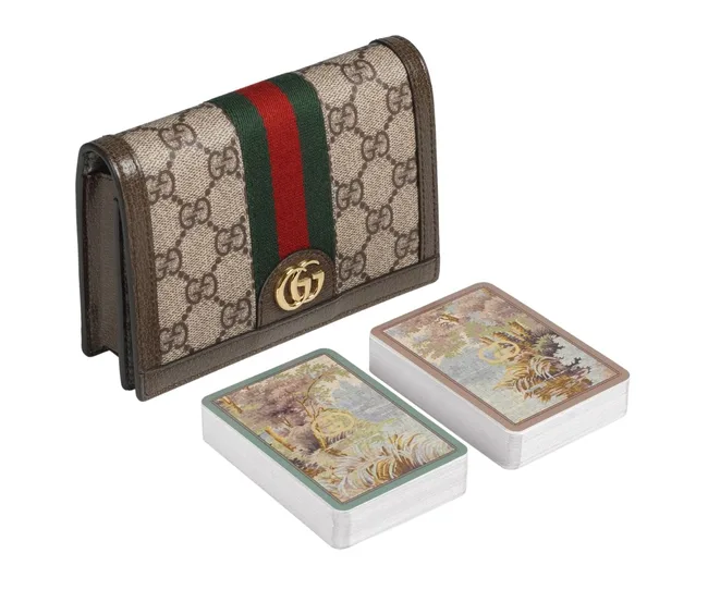 Gucci monogrammed case with green-red stripe and gold logo, alongside two decks of landscape design playing cards.