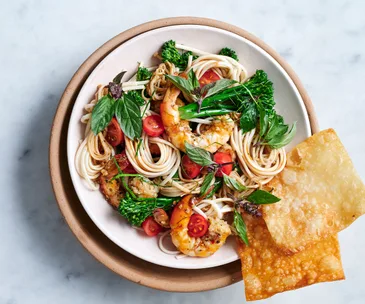Aerial view of a bowl of noodles with prawns, mint and tomatoes.