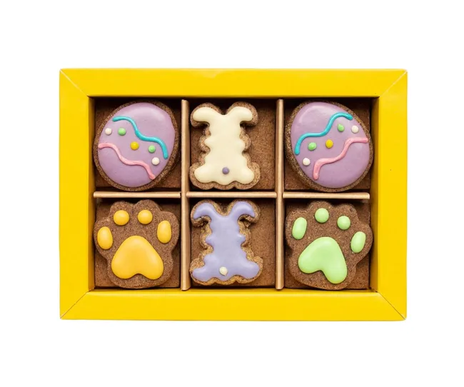 A yellow box with colorful, decorated Easter-themed cookies shaped like eggs, rabbits, and paw prints.