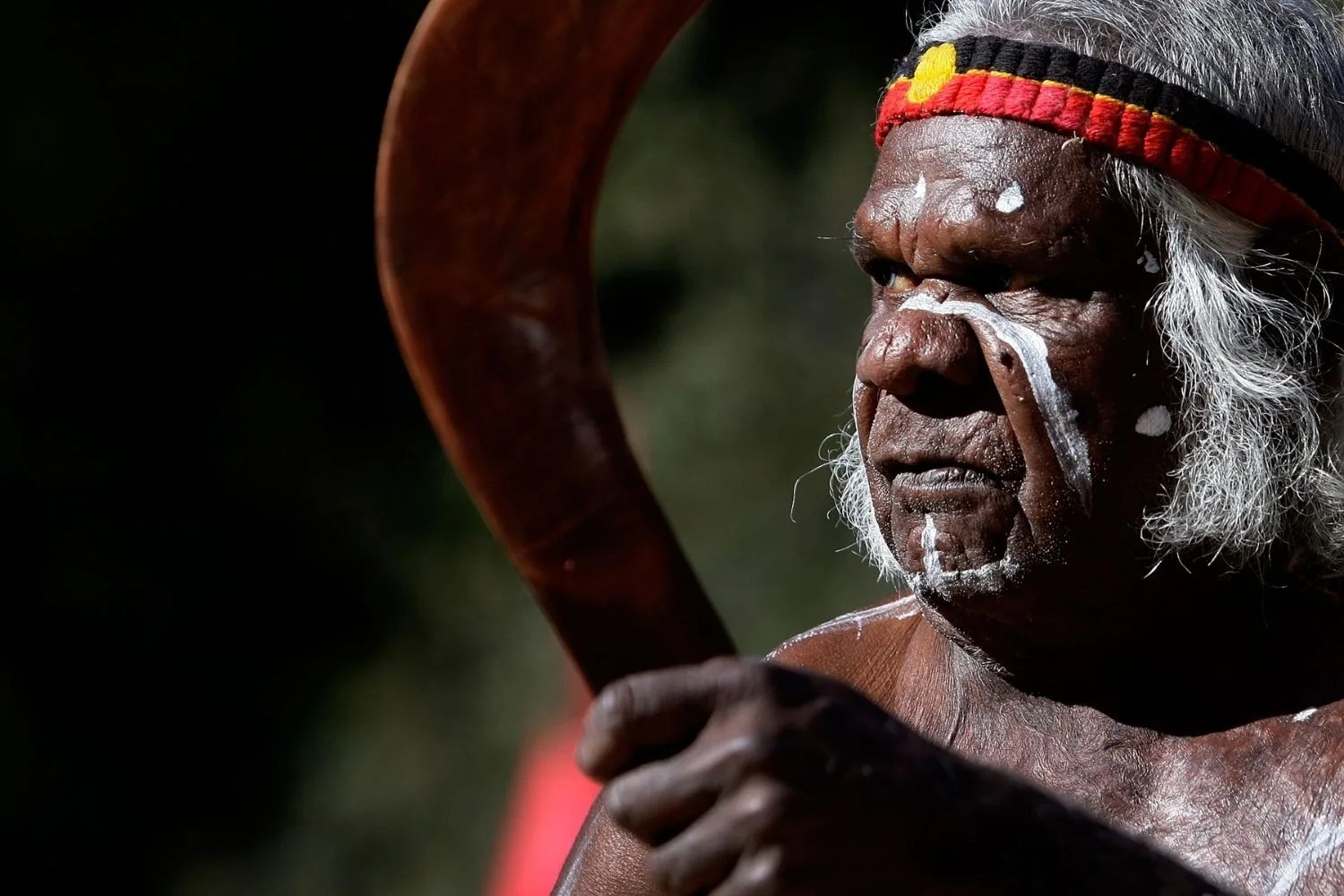 a man with an aboriginal headband, face paint, and holding a boomerang