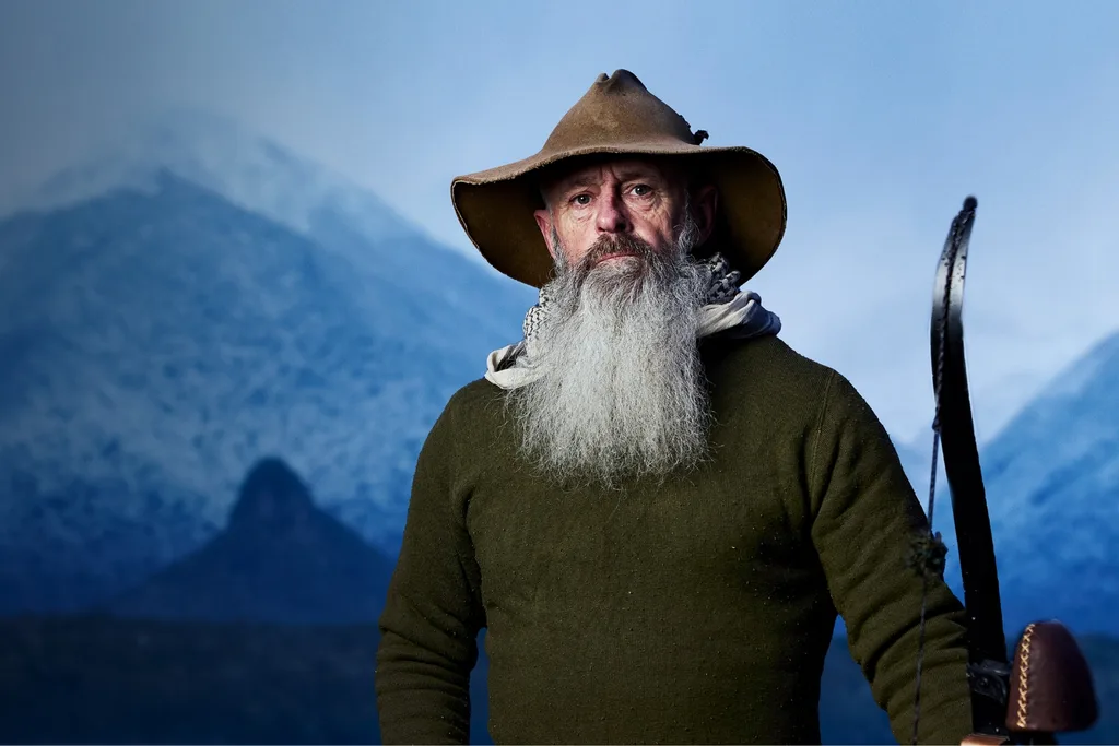 Alone contestant Rick with a long grey beard, wearing a dark green jumper standing outside in a cold environment.