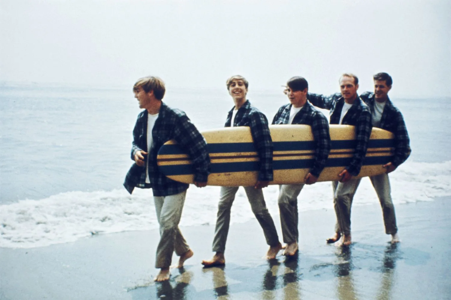 the beach boys holding a surfboard and walking on the beach