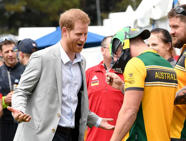 Prince Harry, Duke of Sussex laughs as an Invictus competitor puts a pair of swimming trunks on his head