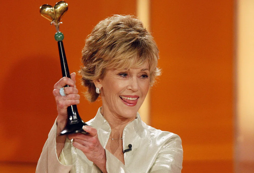 Jane Fonda receives an award in front of an orange background