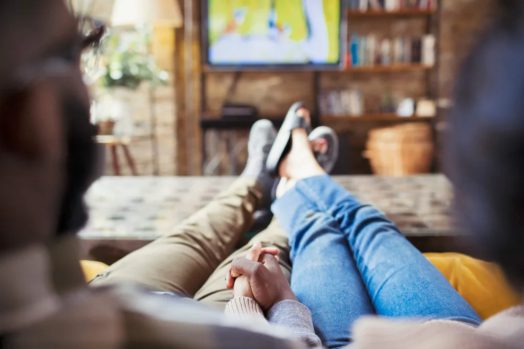 Couple holding hands on couch watching TV