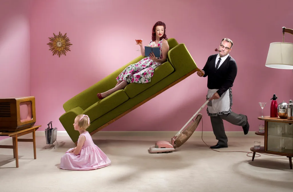 Dad vacuuming pink and green lounge while wife and child relaxes