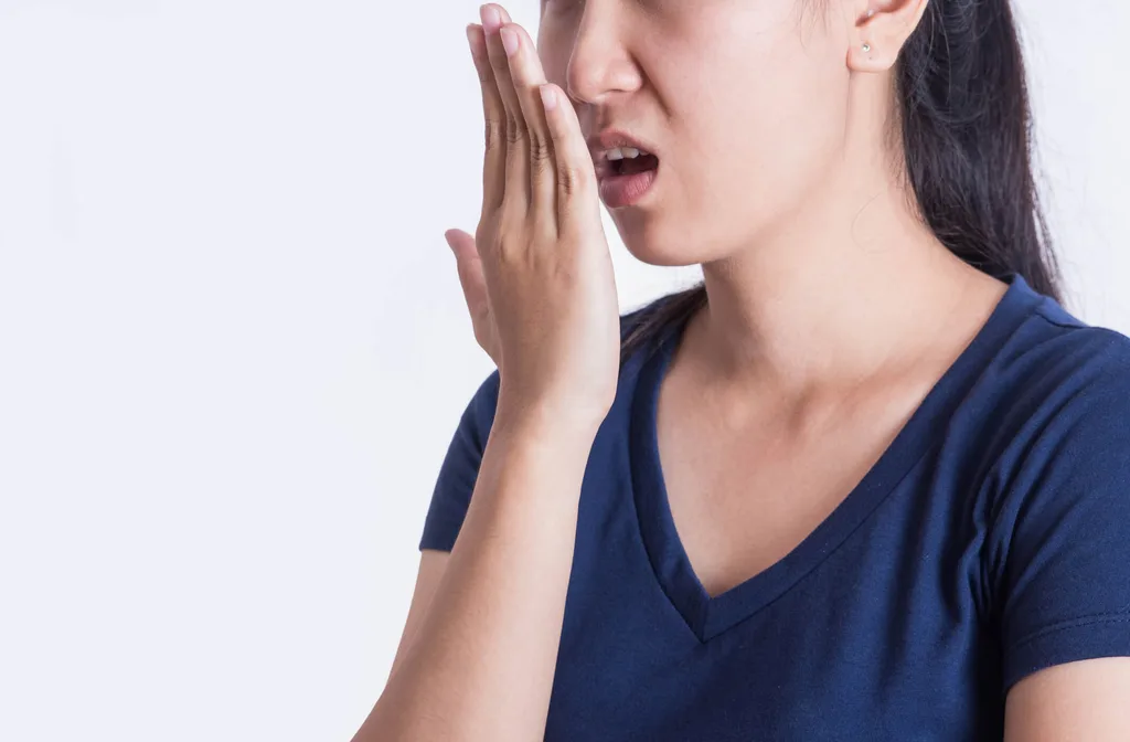 Woman smelling her own breath against hand