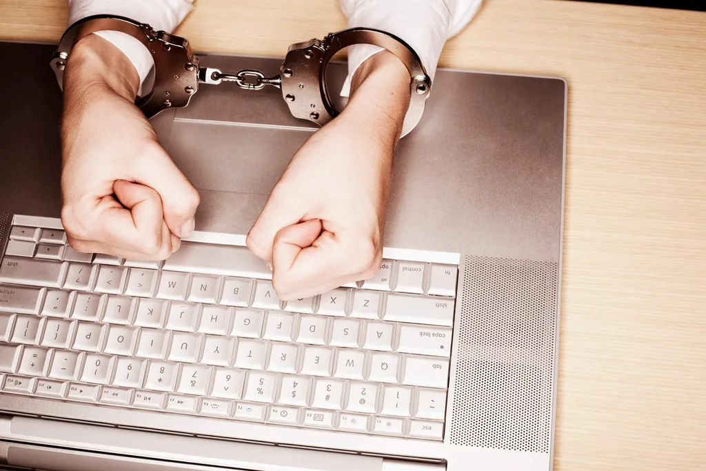 A person's hands handcuffed over the top of an old laptop