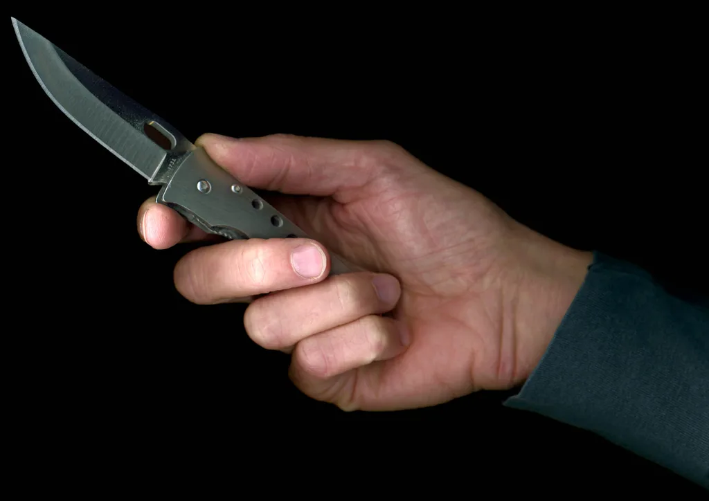 A man holding a pen knife against a black background