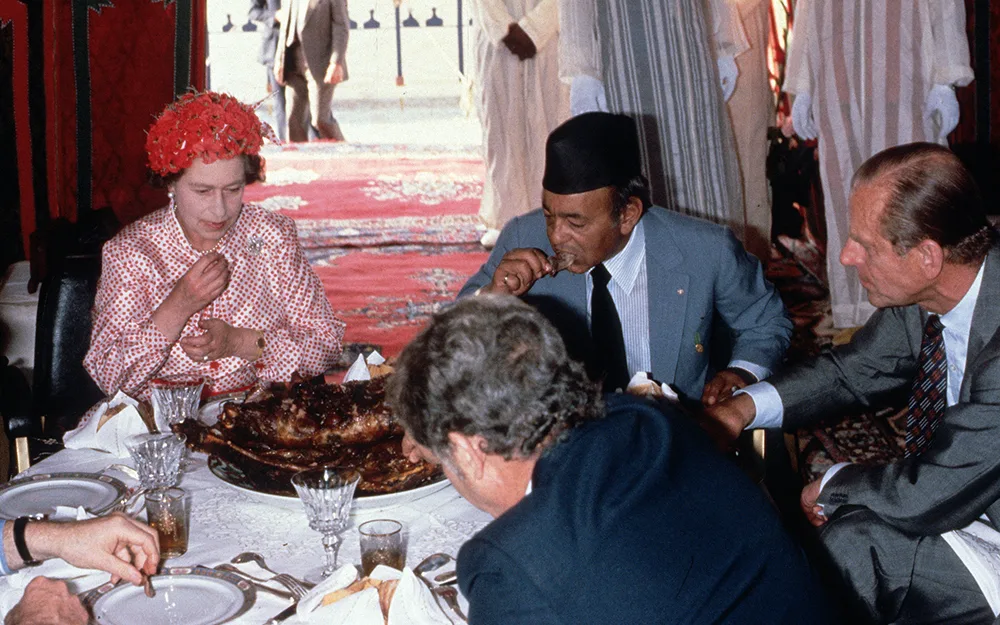 Queen Elizabeth II, Prince Philip, Duke of Edinburgh and King Hassan ll eat with their hands as they attend a feast in the desert on October 27, 1980 in Morocco.