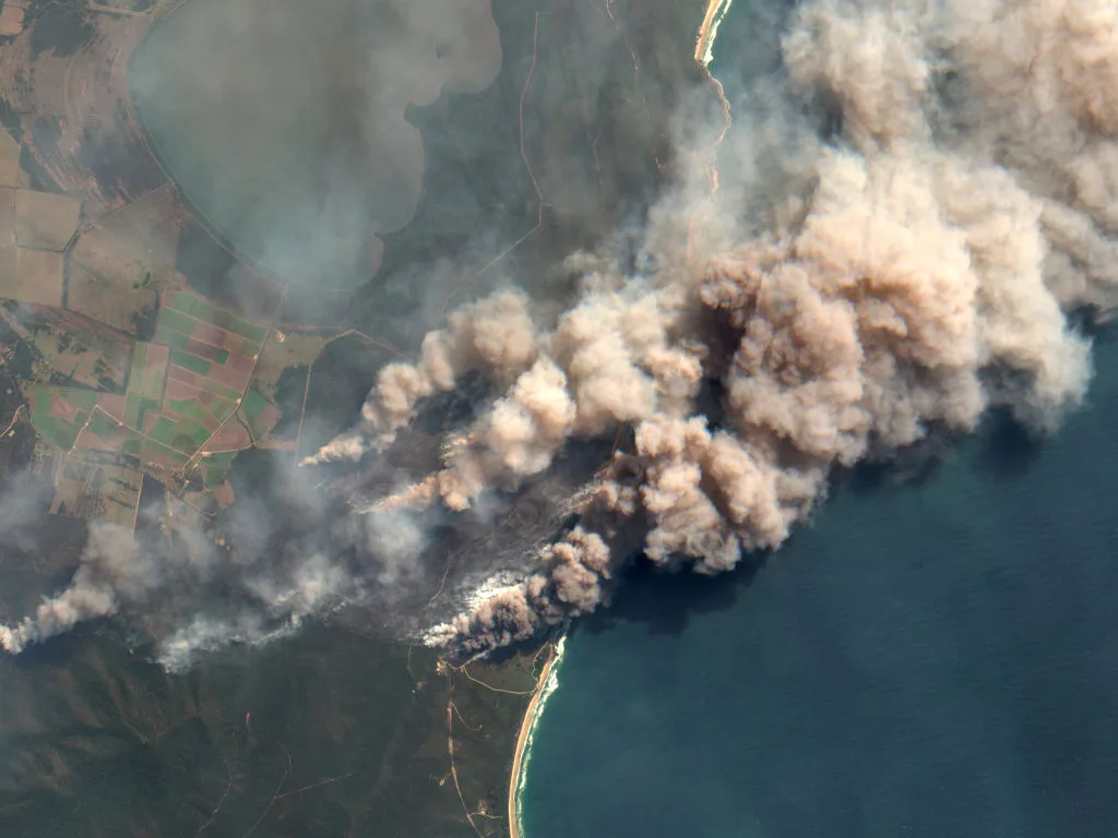 An aerial photo of the Australian coast with bushfire smoke