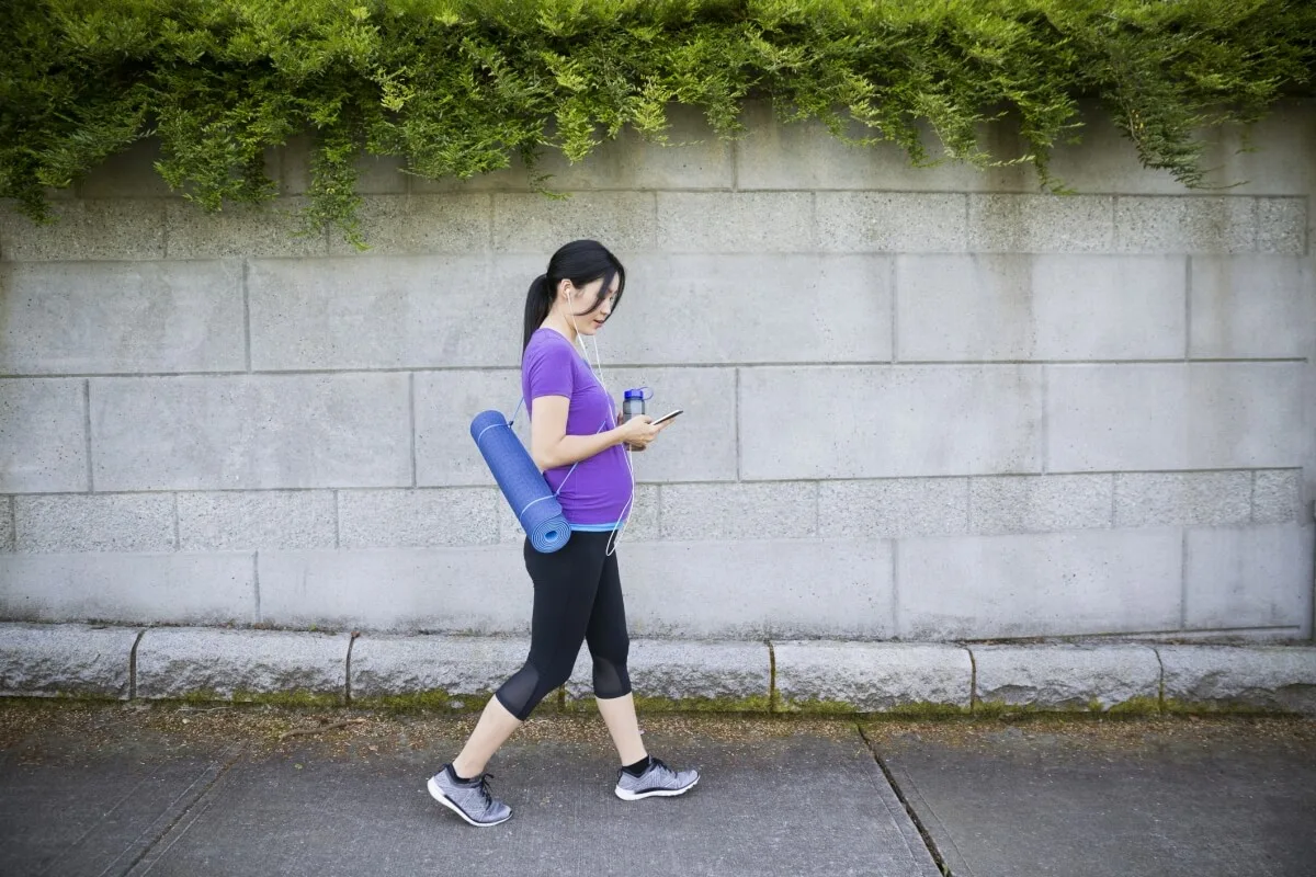 A pregnant woman walking with a yoga mat