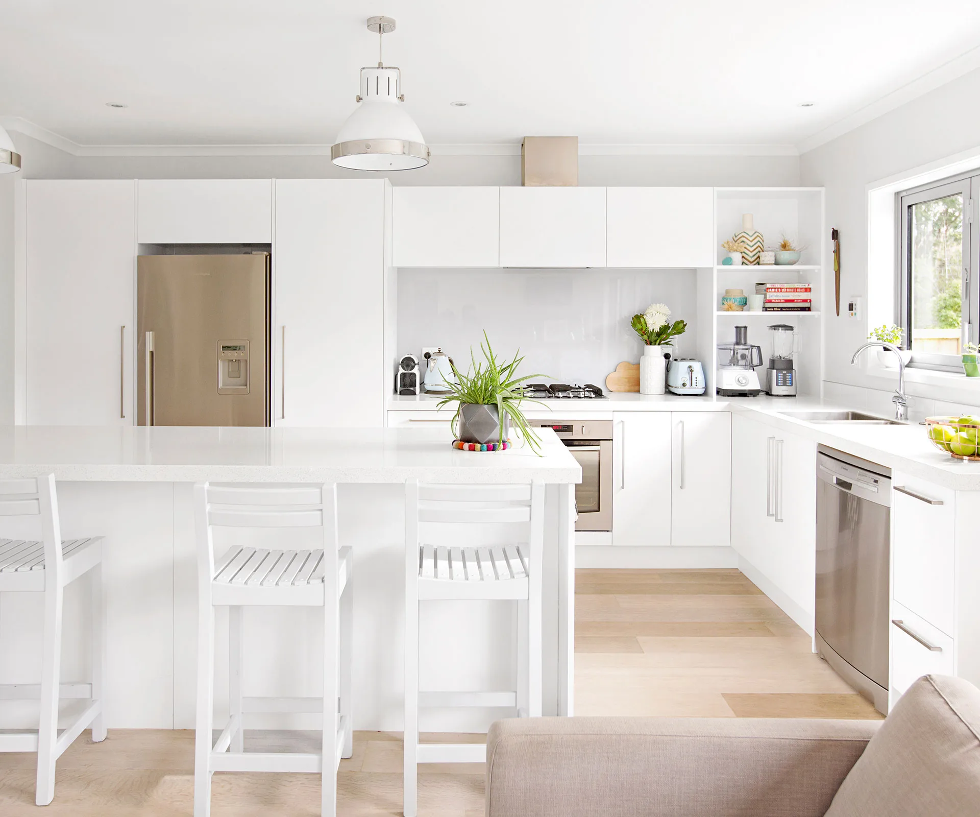 The crisp white kitchen pays homage to its contemporary surrounds, while the white-painted stools and industrial pendant light lend a more casual vibe. 