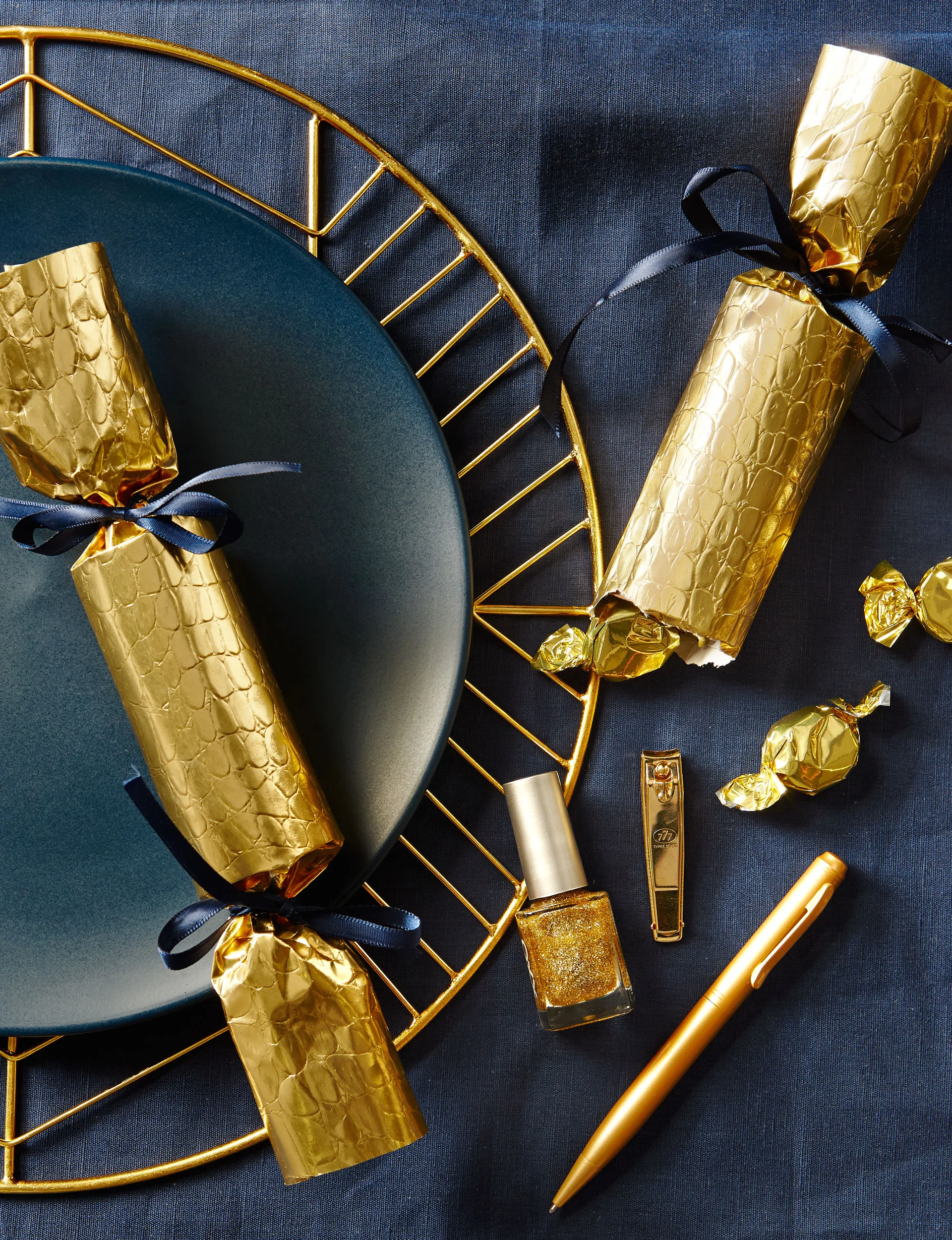 Two golden Christmas crackers on navy-coloured plates. 