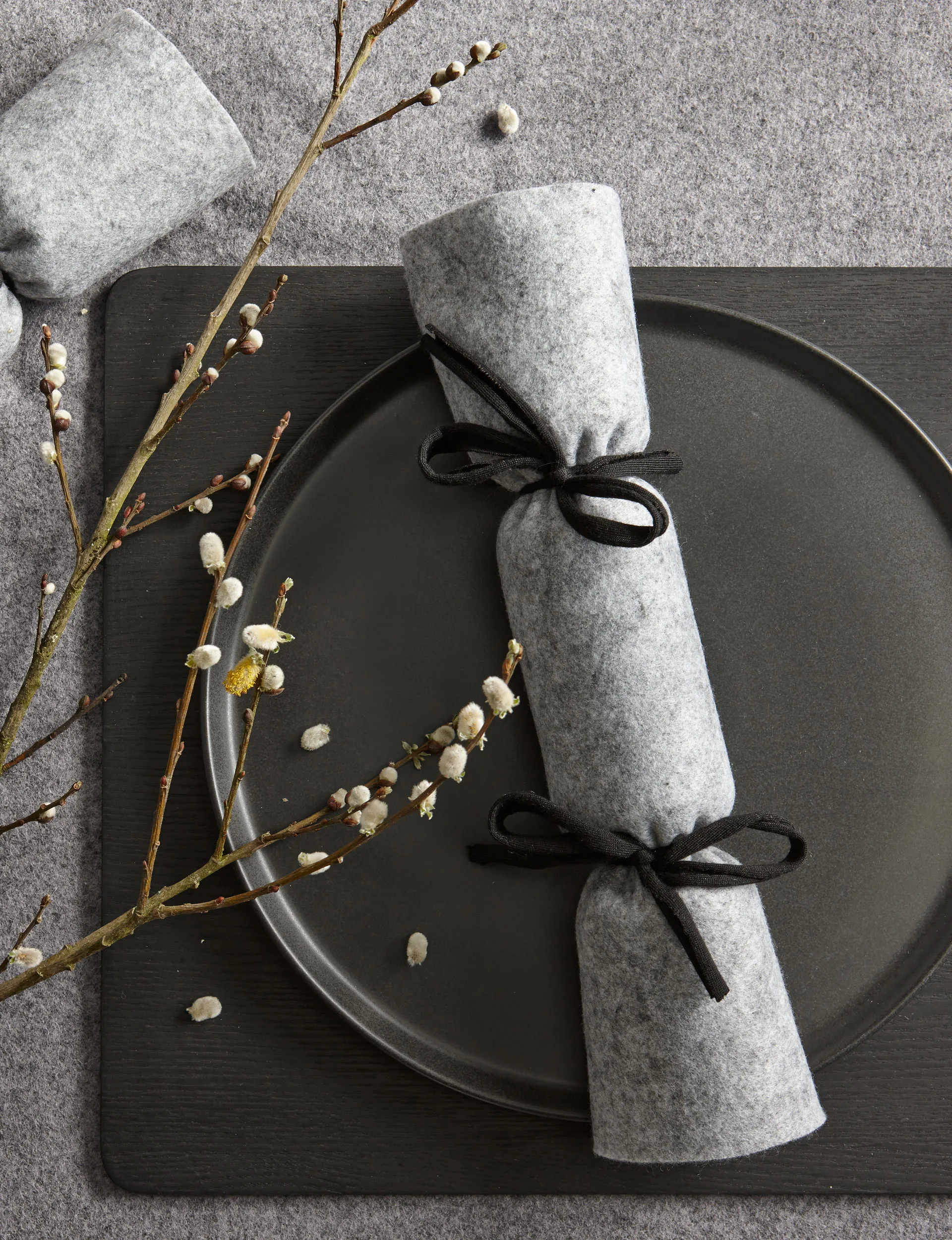 A grey, felt Christmas cracker on a black plate. 