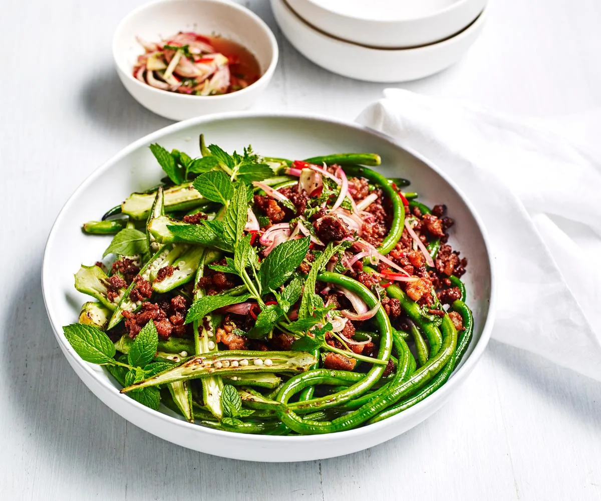 A round white dish with a stir-fry of pork mince, snake beans and sliced okra, topped with mint sprigs.