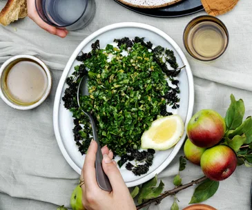 Over-the-top image of an oval white dish with a chopped parsley salad, garnished with a lemon wedge.