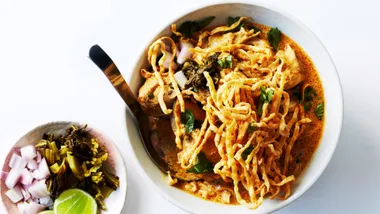 An overhead shot of a vibrant bowl of Khao Soi noodles with a plate of condiments on the side.
