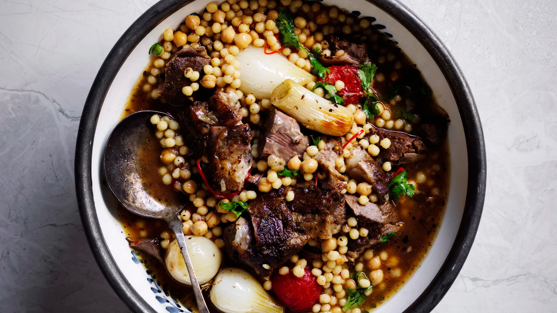 bowl of Baharat lamb shoulder with pearl onions and mogbrabich giant couscous recipe