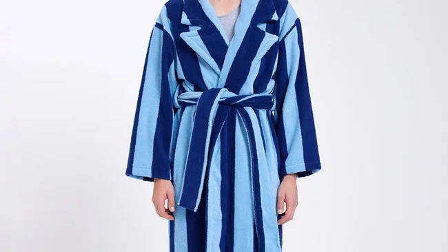 Person wearing a blue and light blue striped bathrobe with a belt, on a plain background.