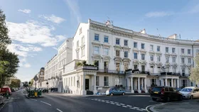 Street view of elegant white terraced Victorian townhouses with parked cars and a blue sky.