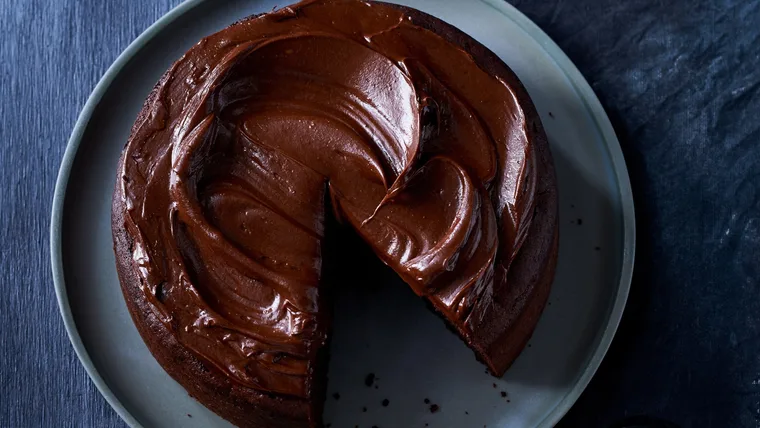 A close up shot of a glossy, fudgy chocolate cake with ganache frosting from above.