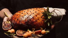 Best christmas hams australia to buy - glazed christmas ham on platter, surrounded by halved blood oranges and whole orange cirtus