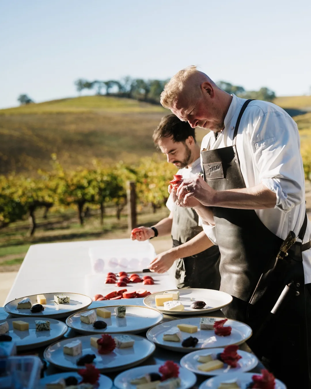 Chefs prepare cheese boards in a pretty outdoor setting in a vineyard.