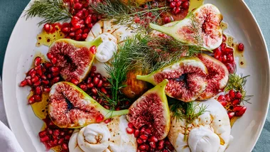 A large plate of figs with burrata, garnished with pomegranate arils and fennel sprigs