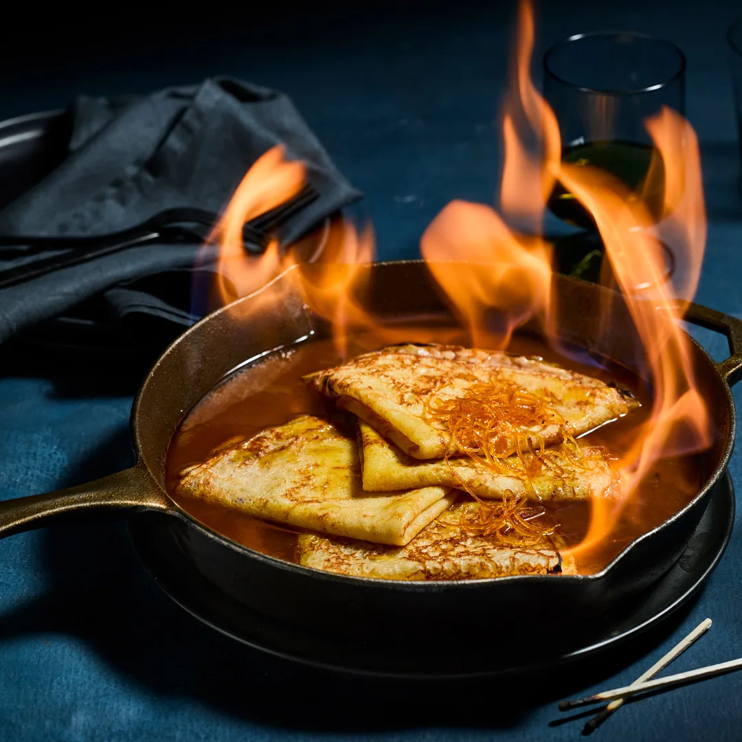 crêpes Suzette in a cast iron pan with candied orange peel and sauce with flames