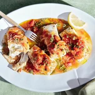 Baked blue-eye trevalla with silver fork on white serving platter with lemon wedge.