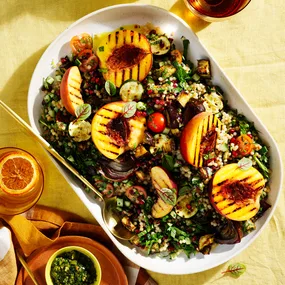 Eggplant with tabbouleh salad with grilled peaches and pomegranate in white dish with a gold spoon and small bowl of tabbouleh.