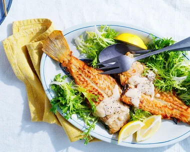 Flounder with avgolemono sauce with salad and lemon on light blue dish with grey cutlery.