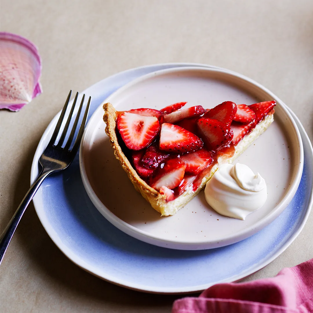 Goats cheese tart with strawberries on white plate with dollop of double cream.