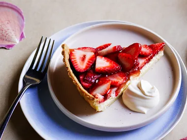 Goats cheese tart with strawberries on white plate with dollop of double cream.