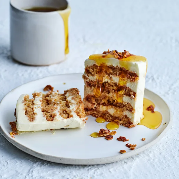 Individual anzac biscuit and mascarpone layer cake with oat crumb on white plate with white mug of golden syrup.