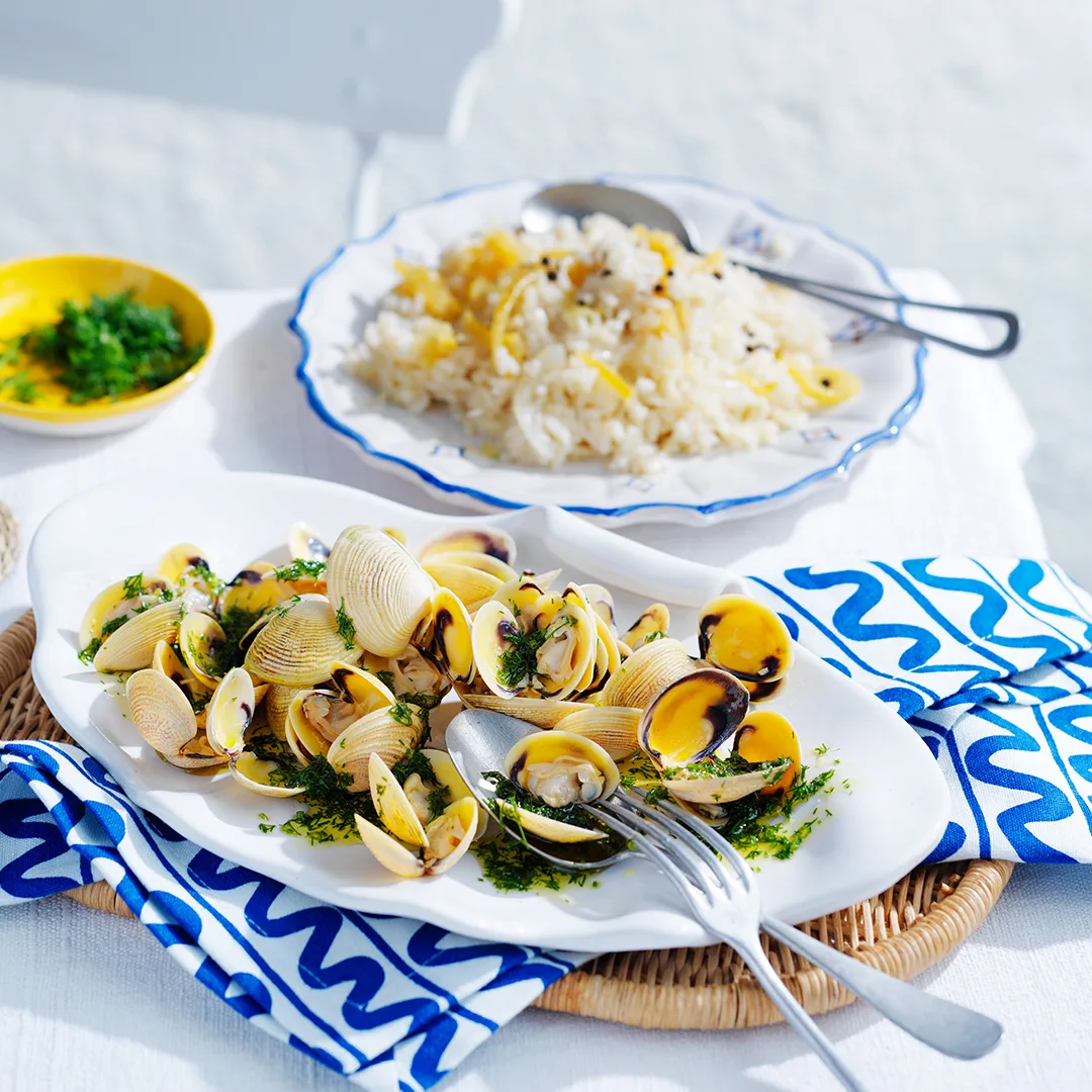 Lemon rice with vongole and dill oil on white dish with blue and white patterned napkin and silver knife and fork.