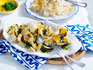 Lemon rice with vongole and dill oil on white dish with blue and white patterned napkin and silver knife and fork.