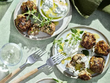 Meatballs served with tzatziki, two silver forks and water glass.