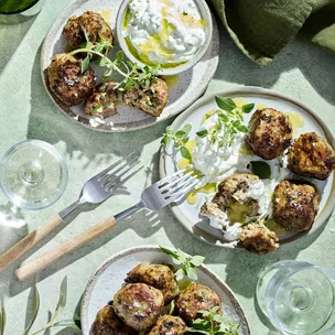 Meatballs served with tzatziki, two silver forks and water glass.