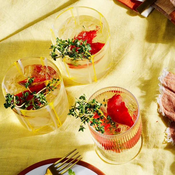 Three Plum and thyme prosecco spritzes with sprigs of thyme in cocktail glass.