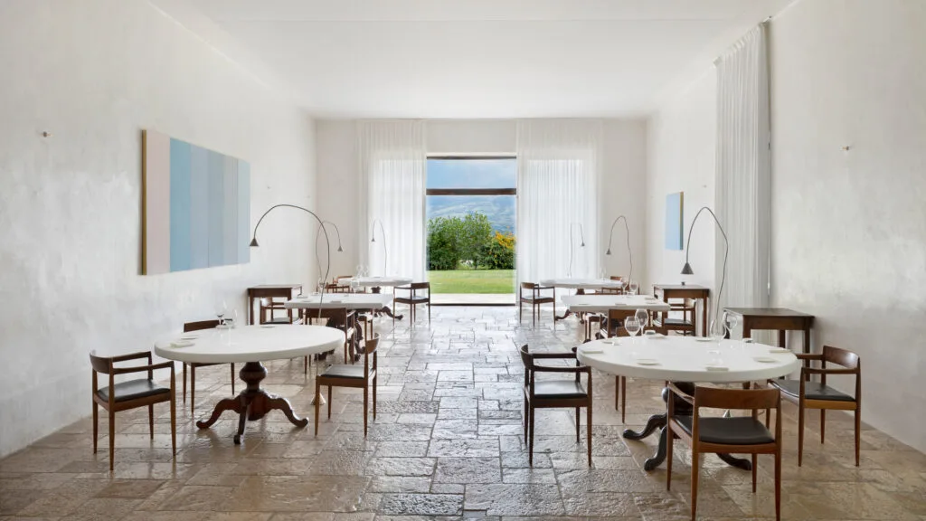 Light, bright dining room with white walls, tiled floor and scenic outlook at Michelin star restaurant Italy, Ristorante Reale.