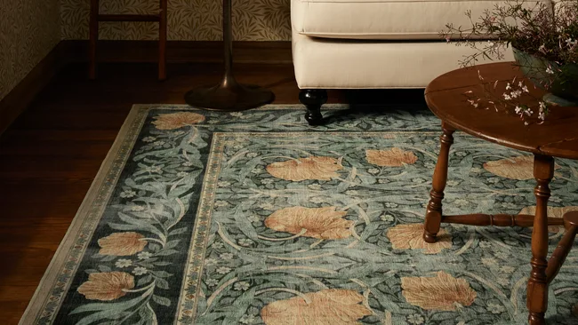 Lifestyle photo showing Ruggable x Morris & Co. blueish green rug with pink flowers with dark timber coffee table