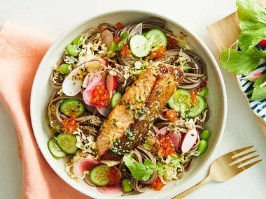 Salmon soba noodle with ginger butter and radish in bowl with orange napkin with gold fork.