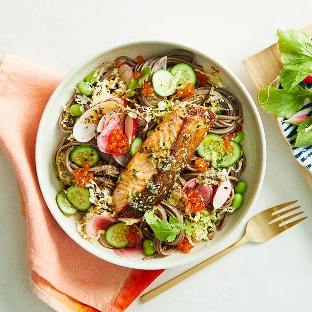 Salmon soba noodle with ginger butter and radish in bowl with orange napkin with gold fork.